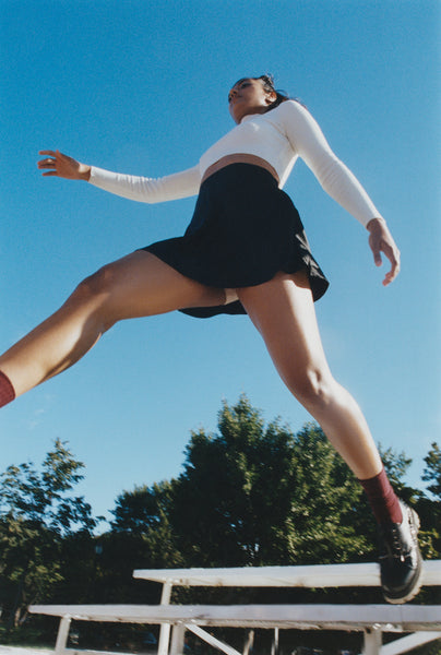 A woman jumping over school bleachers with a blue sky and trees in the background