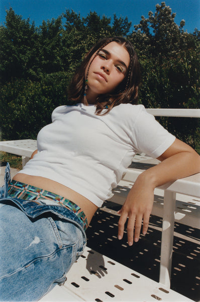 A white woman with her pants slightly unbuttoned to reveal her patterned period underwear relaxes on a set of bleachers outdoors